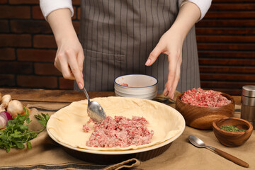 Woman making meat pie at wooden table, closeup
