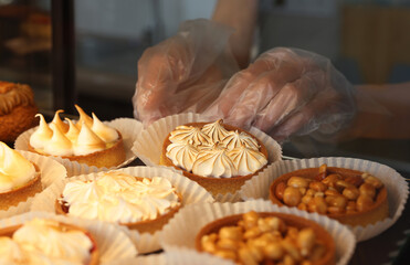 Seller taking tasty tartlet from showcase in bakery shop, closeup