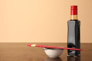 Bottle, bowl with soy sauce and chopsticks on wooden table against beige background. Space for text
