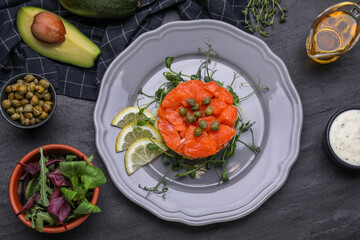 Delicious salmon tartare with microgreens and lemon on dark table, flat lay