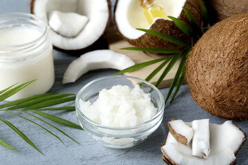 Organic coconut cooking oil, leaves and fresh fruits on grey wooden table, closeup