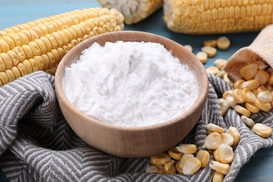 Bowl with corn starch, ripe cobs and kernels on table, closeup