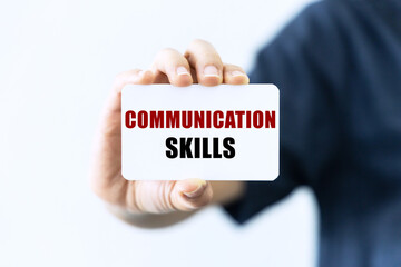 Communication skills text on blank business card being held by a woman's hand with blurred background. Business concept about communication skills.
