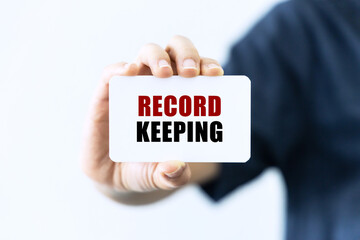 Record keeping text on blank business card being held by a woman's hand with blurred background. Business concept about record keeping.