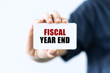 Fiscal year end text on blank business card being held by a woman's hand with blurred background. Business concept about fiscal year end.