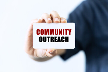 Community outreach text on blank business card being held by a woman's hand with blurred background. Business concept about community outrach.