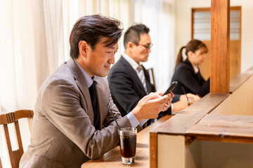 カフェのカウンターでスマホを使うアジア人のビジネスマン
