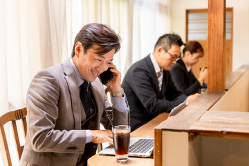 カフェのカウンターでスマホとノートパソコンを使うスーツを着たアジア人のビジネスマン  © buritora