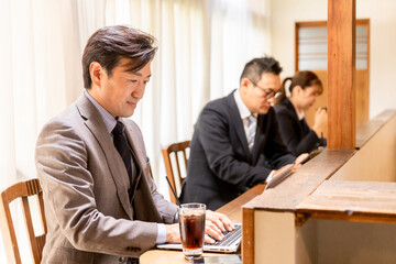 Fototapeta na wymiar カフェのカウンターでノートパソコンを使うスーツを着たアジア人のビジネスマン 