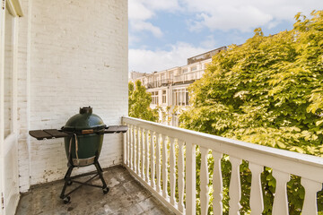 a grill sitting on the porch in front of a white brick building with green trees and blue sky behind it
