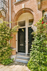 a black door in front of a brick house with green plants and red roses on the steps leading up to it