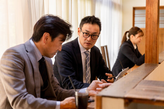 カフェのカウンターで同僚と打ち合わせ・ミーティングをするアジア人のビジネスマン
