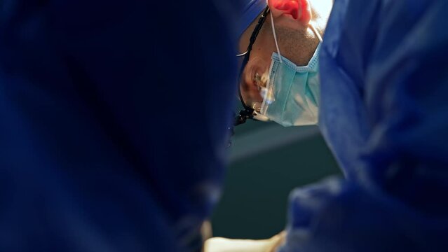 Focused face of a surgeon wearing device glasses. Doctor performing neurosurgery at operational room. Low angle view.