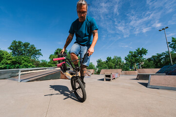 A professional middle-aged tattooed bmx rider is doing practice for the X-games in the skate park.