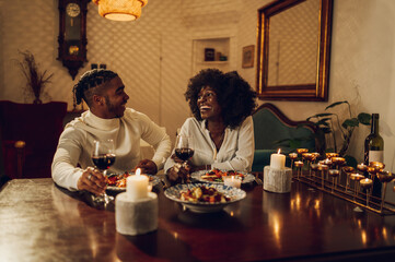 Fototapeta na wymiar African american couple having romantic dinner date and drinking wine at home