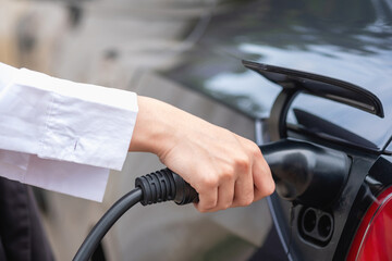 electric car or EV charging station A woman plugs in a black power cable to charge for clean energy...