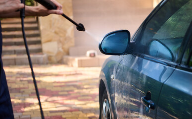 Naklejka premium Manual car wash with pressurized water outdoor. Man cleaning, washing vehicle using high pressure water jet in summer. High pressure cleaning equipment, compressor. Car detailing. Hand washer, cleaner
