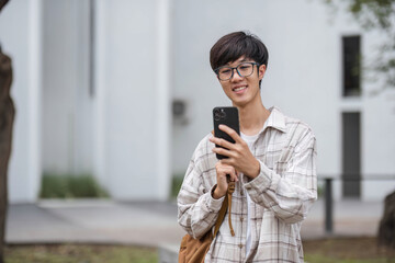 asian male college student with smart phone on sunny campus