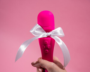 Woman holding pink vibrator with white bow on pink background. Copy space. 