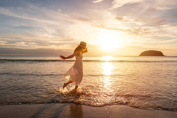 Young woman traveler dancing and enjoying beautiful Sunset on the tranquil beach, Travel on summer vacation concept
