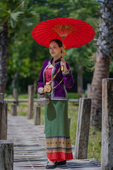 Obraz premium Beautiful pretty young Asian woman wearing a millionaire traditional Thai dress Lanna style standing with an antique silver bag and umbrella in a green natural park.