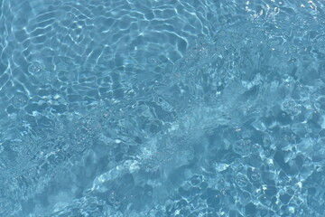 Blue water with ripples on the surface. Defocus blurred transparent blue colored clear calm water surface texture with splashes and bubbles. Water waves with shining pattern texture background.