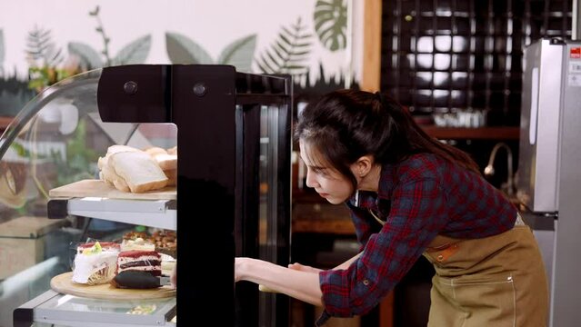 Close-up, cafe worker is opening bakery cabinet, bent down use tongs pick cake in refrigerator out put them on sall tray, that is served customers who order eat in store, close cabinet when finished.