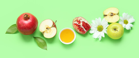 Ripe pomegranates, apples, flowers and honey on green background. Rosh Hashanah (Jewish New Year) celebration