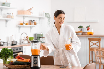 Young woman with glass of vegetable juice and blender in kitchen
