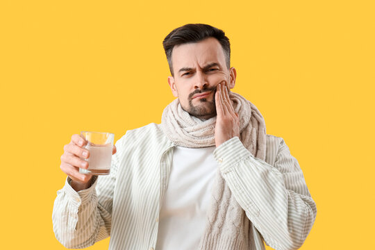 Ill young man with dissolved tablet in glass of water on yellow background