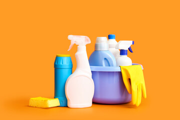 Bowl with different cleaning supplies on orange background