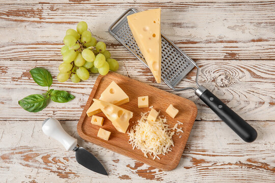 Board with tasty Swiss cheese and grapes on light wooden background
