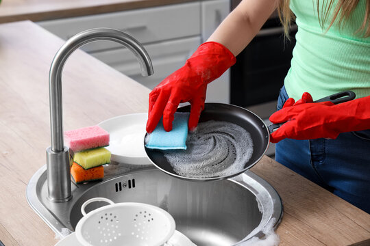 Woman in red rubber gloves washing frying pan with sponge - Powered by Adobe