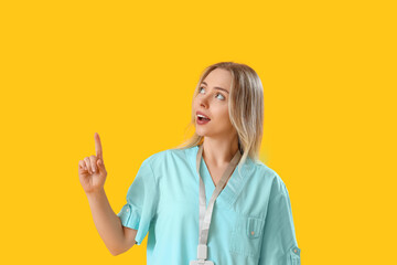 Female medical intern pointing at something on yellow background