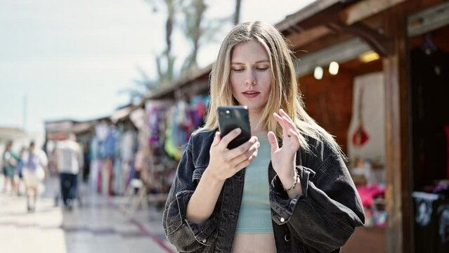 Young blonde woman smiling confident making selfie by the smartphone at street market