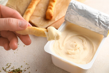 Woman eating tasty grissini with cream cheese on light background