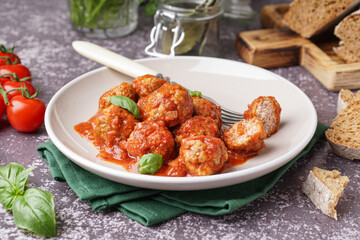 Plate of tasty meat balls with tomato sauce and basil on grey background