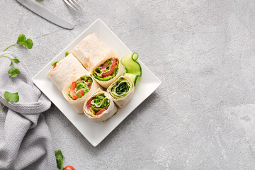 Plate of tasty lavash rolls with vegetables on grey background