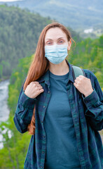 Young woman wearing face mask during coronavirus and flu outbreak stands at mountains