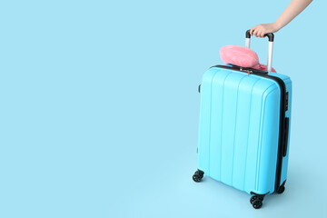Female hand with suitcase and travel cushion on blue background. Travel concept