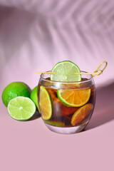 Glass of cold Cuba Libre cocktail on lilac background