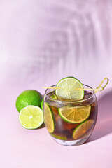 Glass of cold Cuba Libre cocktail on lilac background