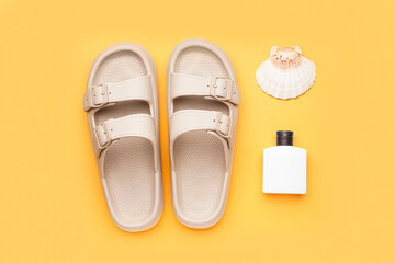 Beige flip-flops with bottle of sunscreen cream and shell on orange background