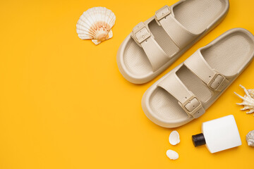 Beige flip-flops with bottle of sunscreen cream and shells on orange background