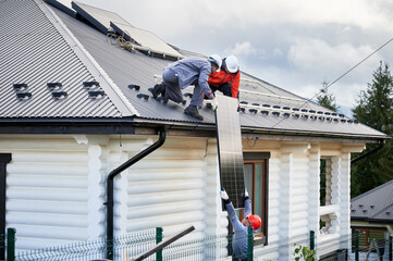 Men mounters installing solar panel system on roof of house. Workers in helmets lifting up...