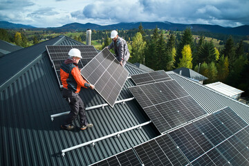 Workers building solar panel system on roof of house. Men technicians in helmets carrying...