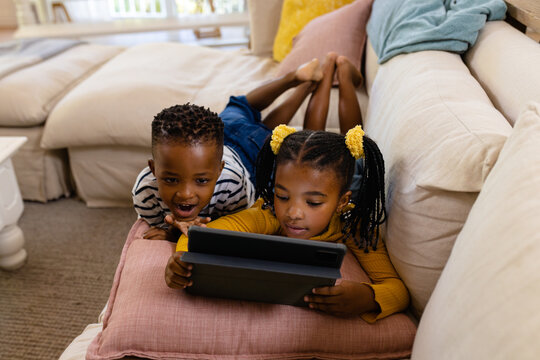 High angle view of african american siblings using digital tablet while lying on sofa in living room