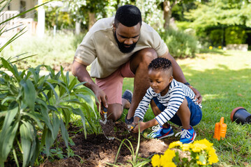 African american father assisting son in digging dirt with tools on grassy field in backyard