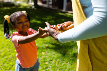 Midsection of african american mother holding daughter's hands in backyard on sunny day