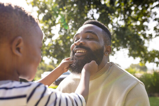 African american cheerful son holding father's beard while playing in backyard during weekend